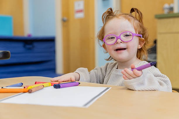 A smiling toddler with crayons and paper