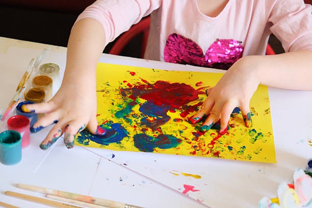 A child finger-painting on yellow paper